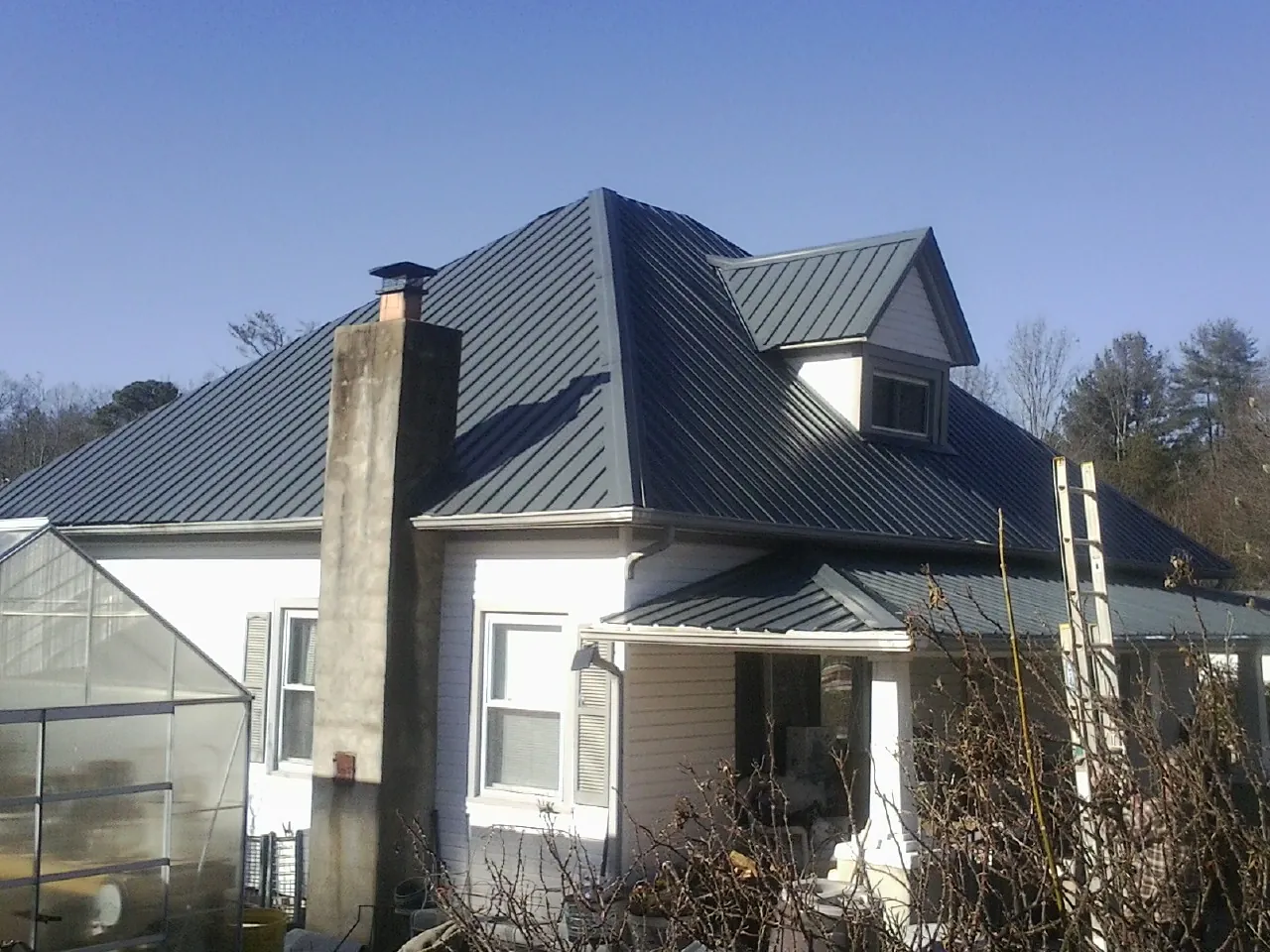 Dark blue standing seam metal roof on a white farmhouse with dormer — Slate & Tile Roof Repair by Roofing Brothers in Dellrose