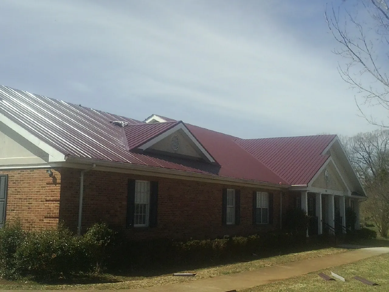 Red metal roof with gabled entries on a long brick building, from a Hail Damage Roof Repair job in Dellrose