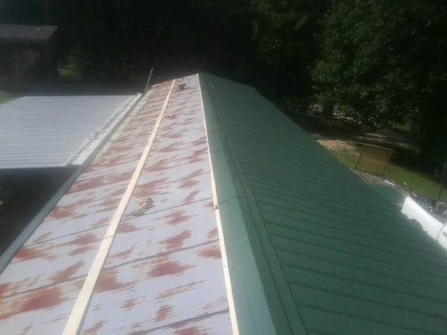 Old rusted panels beside newly installed green metal roofing — Wind Damage Roof Repair by Roofing Brothers in Dellrose