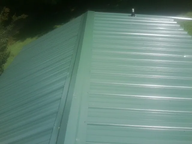 New green metal panels meeting at the ridge of a roof — Flat Roof Repair work by our crew in Dellrose