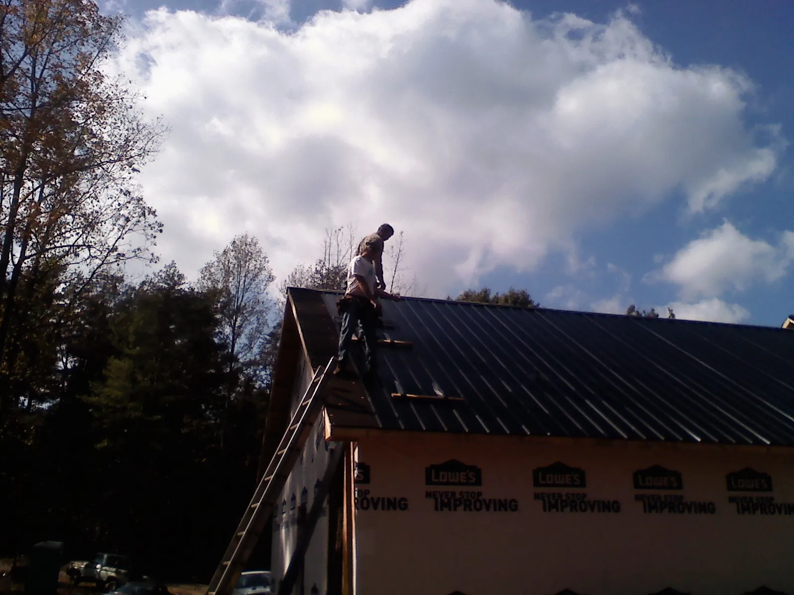 Roofer fastening dark metal panels high against a cloudy sky, from a Roof Inspection job in Dellrose