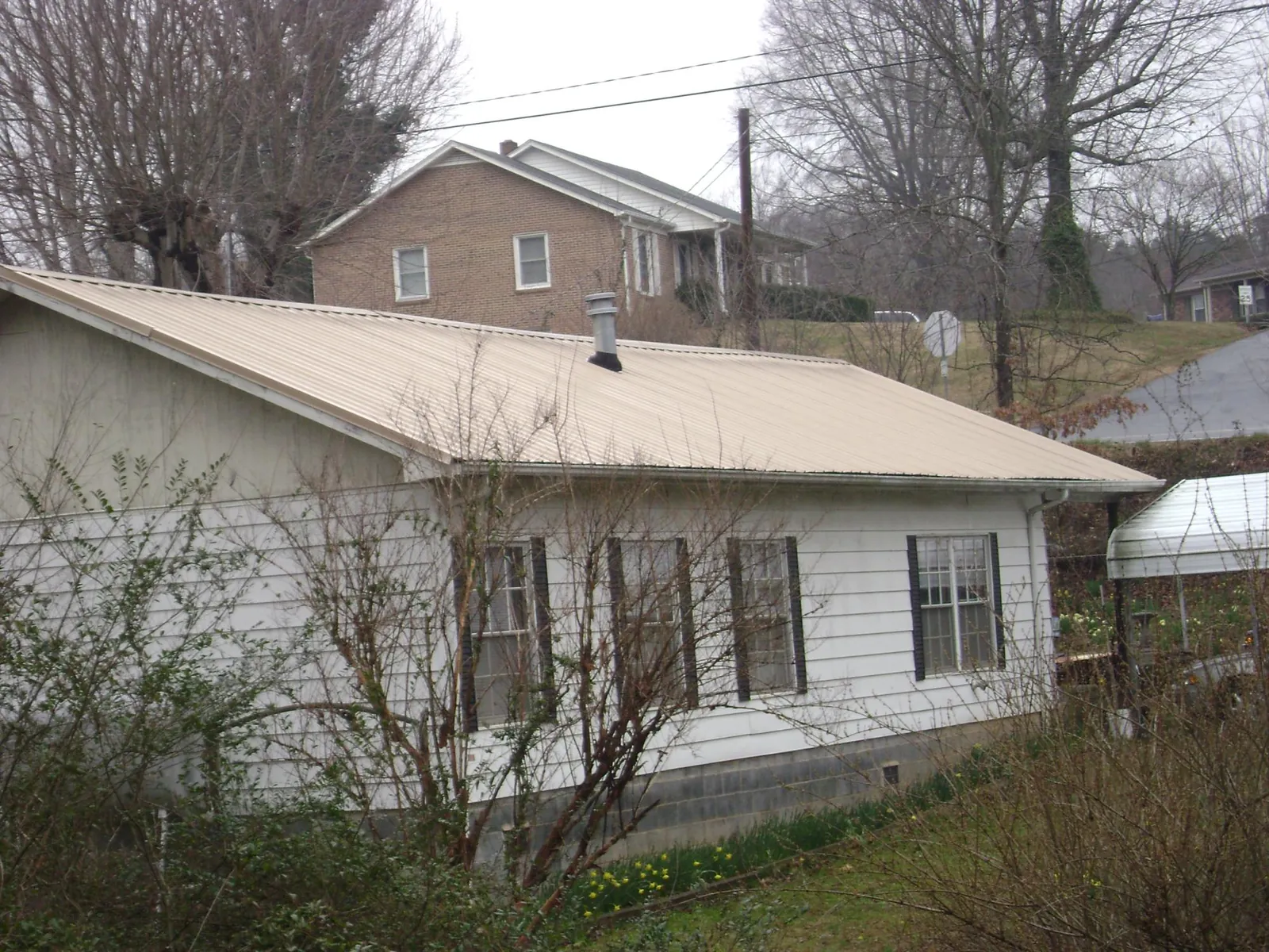 Tan metal roof on a white sided house set into a hillside — Commercial Roofing by Roofing Brothers in Dellrose
